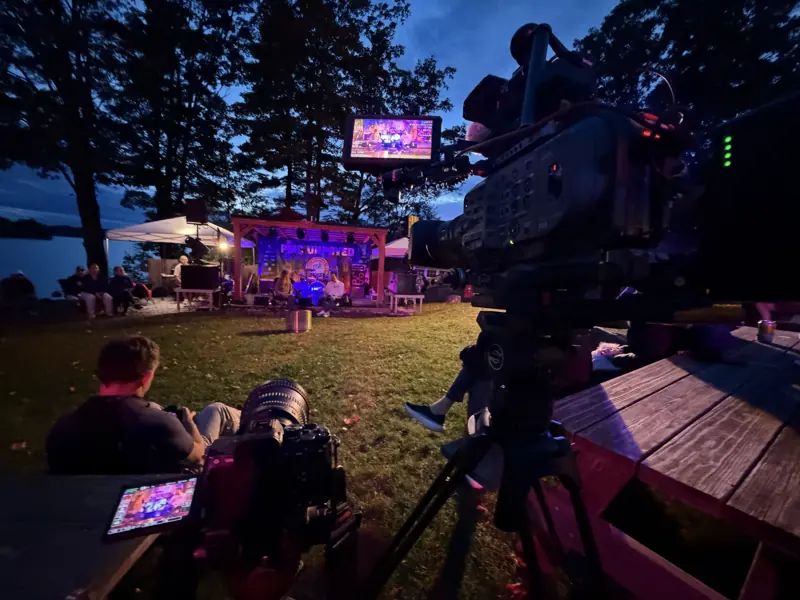 The Sony FX9 in the foreground and the PMC Unpaved stage lit purple across the lawn at blue hour